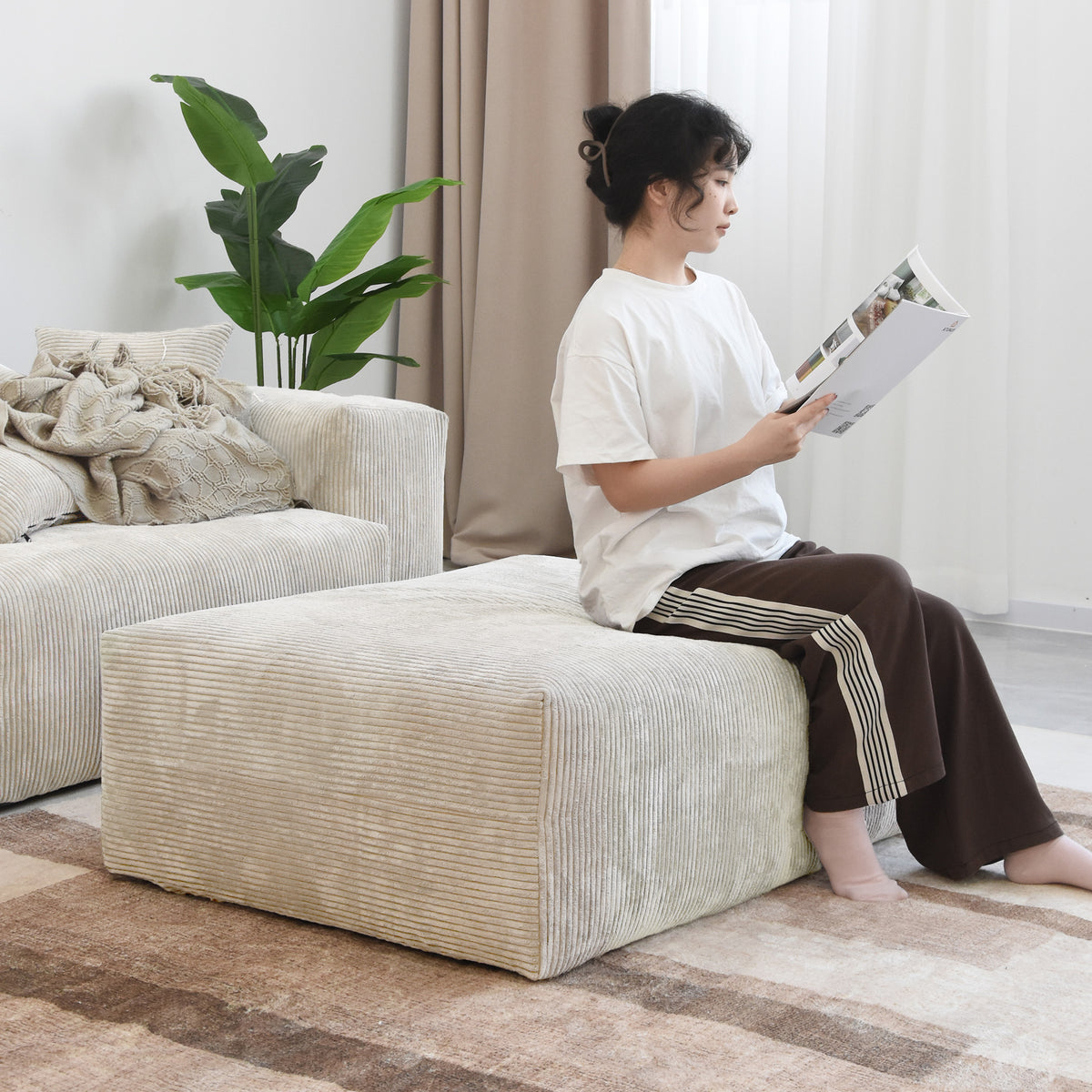 A person sitting on a beige corduroy ottoman module reading a magazine beside the matching sofa